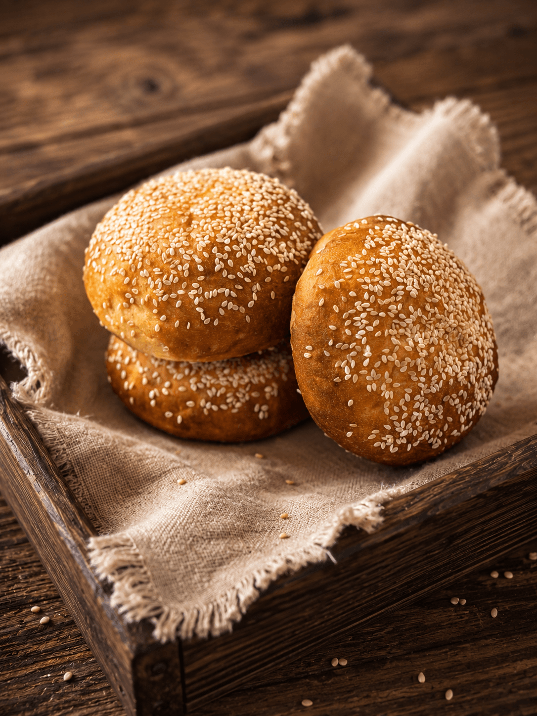 Sesame buns resting in a linen-lined wooden tray